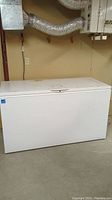 White large Frigidaire chest freezer closed, placed in basement with visible ductwork above.