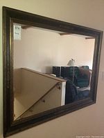 Full view of the large framed mirror showing reflection of a staircase and living room chairs.