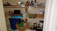 Overall view of three shelves holding the office supplies including desk lamp, recycle bin, file folders, staplers, bookends, compass set, phones, and shredder.