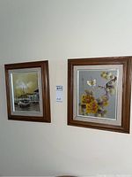 Photo of two framed paintings on a wall, one ship scene on left, floral on right