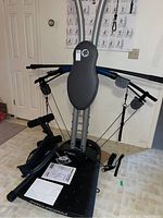 Photo of the ProForm Recoil exercise machine showing metal frame, padded backrest, resistance cords, footrests, and manuals placed on the base platform.