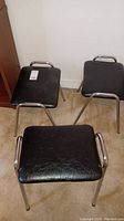 Three black leatherette stacking stools with chrome metal legs arranged in a triangle on carpet.