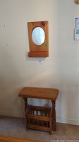 Wall-mounted wood frame mirror with small bin for holding items, oval mirror surface.
