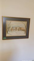Framed watercolour painting hanging on wall depicting a winter scene with a house and trees.