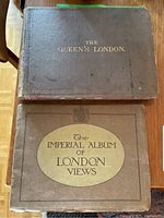 Two closed hardcover photo books lying flat on a wooden surface, showing the front covers with titles The Queen's London and The Imperial Album of London Views.