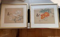 Two Asian style paintings side by side in square metal frames with glass, showing butterflies and flowers on tan background.