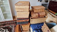 Photo of stacked wicker baskets, picnic baskets with leather straps, and a wooden box in a pile.