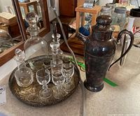 Full cruet set on a round plated silver tray, includes oil and vinegar bottles with stoppers, salt and pepper shakers, cordial glasses, and a tall carafe.