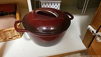 Red enamel Kitchen Aid Dutch oven with lid on white shelf