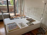 Full view of assembled white metal bed frame with mattress and assorted framed artwork on top