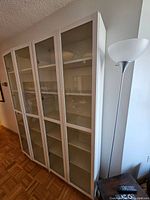 Single white Billy bookcase with glass door next to floor lamp and side table