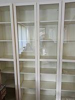 Front view of multiple white Ikea Billy bookcases lined up side by side, glass-panel doors visible