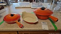 Five-piece set of Le Creuset cookware with two pots, two lids, one frying pan, and one ceramic baking dish photographed on kitchen counter.