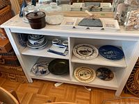 Full cabinet showing various decorative plates on shelves, ceramic container on top with glass domes and vases reflected in mirror