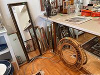 Six wall mirrors in a room environment showing large rectangular and round cane framed mirrors leaning on floor