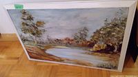 Framed landscape painting on floor showing river or pond scene with trees and sky, signed lower right 'D Gorman 70'.
