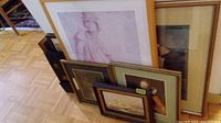 Various framed art prints arranged leaning against wall and each other, includes a large pastel woman sketch and smaller framed prints.