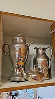 Shelf display of all three items: coffee percolator, teapot, and pitcher.