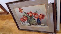Framed watercolour painting of red-orange tulips in a green vase and a blue vase, resting on a surface with a shadow cast.