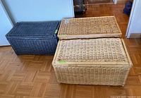 Three wicker storage boxes of varying colors and sizes placed on hardwood floor near wall.