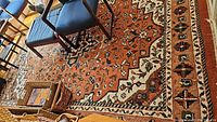Full view of rust-orange wool rug under dining chairs on hardwood floor