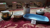 Image showing all five items: green and yellow lemon pitcher and bowl, blue serving platter, brown and beige whiskey jug, and ceramic bean pot with lid on carpet.