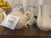 Two cream-colored Belleek porcelain teapots with ribbed design and ornate handles, placed on a wooden surface.