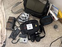 Wide view of the lot containing multiple Canon PowerShot cameras, camera cases, and accessories on carpeted floor.