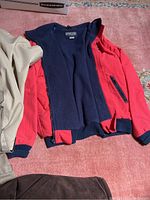 Columbia red jacket opened showing navy fleece lining, with beige raincoat partially visible