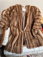 Full view of the mink fur coat laid on a chair showing front and sleeves detail.