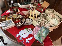 Photo showing Christmas tree dinnerware set with plates, bowls, dishes, some boxed and some out, alongside Christmas stockings, assorted cloth decorations and a music box