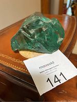 Front angle view of a natural aqua blue Andara crystal on a wooden surface with auction card showing lot number 141.