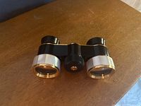 Side view of compact opera binoculars showing black body and mother of pearl decor around lenses.