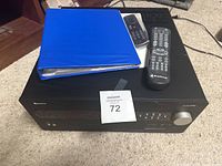 Photo of Outlaw Model 990 preamplifier with two remotes and blue binder on top, showing front panel and knobs.