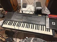 Technics KN400 electronic keyboard with keys and control panel visible, placed on a table with cables around.