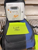 Photo of silver Sony Net MD Walkman CD player sitting on top of a black and blue soft carry case with a yellow sticky note stating 'Lot 30'.