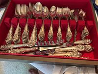 Red velvet lined wooden box bottom with sets of dinner forks, tablespoons, salad forks, teaspoons and one slotted serving spoon