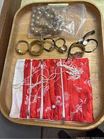 Watches and accessories laid on a wooden tray with red puff fabric organizer pouch containing compartments and strings, showcasing five watches and a metallic bead necklace/bracelet in plastic bag.