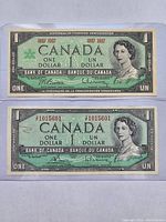 Front side of two Canadian one dollar bills from 1967 and 1954 in protective sleeves showing portraits of Queen Elizabeth II and serial numbers.