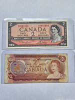 Front sides of the two Canadian $2 bills in protective sleeves showing serial numbers and portraits of Queen Elizabeth II.