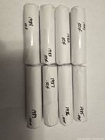 Top view of 8 white paper rolls of pennies labeled with years 1980s except missing 1980 and 1988, showing 50 cent denomination each