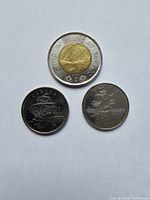 Three Canadian commemorative coins laid out showing front and back designs including a 2012 two-dollar coin and two one-dollar coins with commemorative images