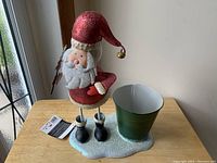 Full view of the Santa Claus figurine decoration standing on a glittery white base with a green metal planter attached.