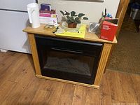 Front view of electric fireplace in wooden mantel frame with various items on top (excluded).