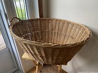 Photo of a large round wicker basket with loop handles on a wooden stool near a door.