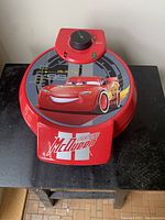 Closed view of red Lightning McQueen themed waffle maker with temperature dial and indicator lights on top.