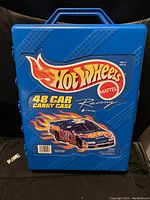 Front view of blue Hot Wheels carrying case labeled for 48 cars, featuring racing car graphic and 'Mattel' branding.