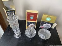 Three crystal jar pieces on a black table with their original boxes behind.