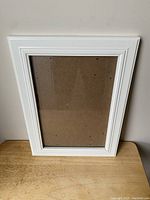 Front view of white picture frame showing border, glass, and backing secured with metal clips.
