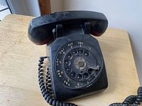Black rotary dial Bell telephone on wooden table, showing front and top with handset resting on cradle.